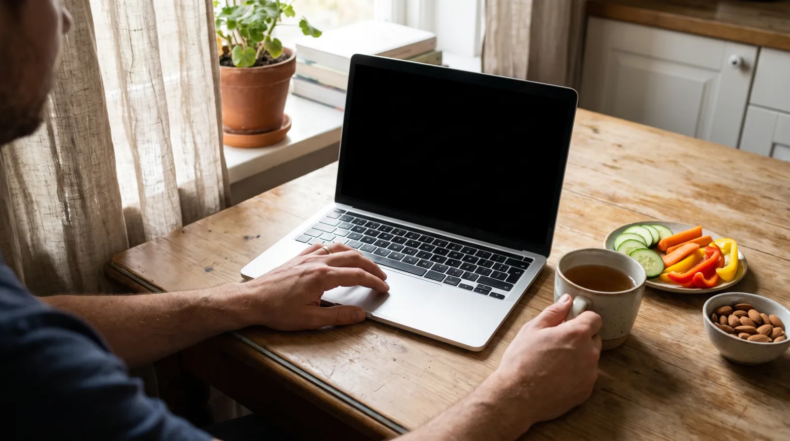 Person am Küchentisch beantwortet am Laptop einen Vitamin Mangel Test online, daneben Gemüse, Nüsse und Tee